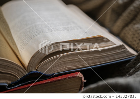 Open old book with weathered pages lying on a rustic knitted blanket representing education and knowledge 143327835