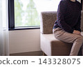 A woman is sitting on a couch, talking. The room is bright, with a window. 143328075