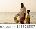 African American father and child walking on beach with swim ring 143328557