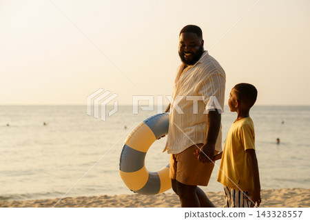 African American father and child walking on beach with swim ring African American father and child walking on beach with swim ring 143328557