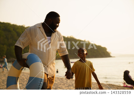 African American father and child walking on beach with swim ring African American father and child walking on beach with swim ring 143328559