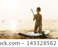Black woman kneeling on paddleboard holding paddle in ocean water 143328562
