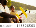 Black father sitting with son on beach talking during sunset 143328563