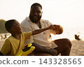 Black father sitting with son on beach talking during sunset 143328565