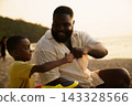 Black father sitting with son on beach talking during sunset 143328566