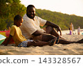 Black father sitting with son on beach talking during sunset 143328567