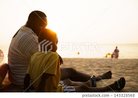 Black father sitting with son on beach talking during sunset Black father sitting with son on beach talking during sunset 143328568