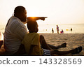 Black father sitting with son on beach talking during sunset 143328569