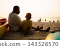 Black father sitting with son on beach talking during sunset 143328570