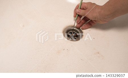 Hook removes bathtub blockage with manual drain cleaning technique. Hook removes bathtub blockage with manual drain cleaning technique. 143329037