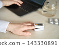 Pulse Oximeter Measuring Fingertip Oxygen Saturation On Hand Beside Laptop And Glass Of Water 143330891