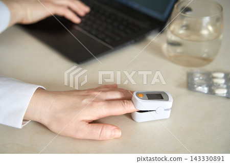 Pulse Oximeter Measuring Fingertip Oxygen Saturation On Hand Beside Laptop And Glass Of Water Pulse Oximeter Measuring Fingertip Oxygen Saturation On Hand Beside Laptop And Glass Of Water 143330891