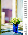Sunlit lily of the valley bouquet in a blue cup on a rustic window sill against a blurry city. 143332225