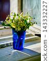 Sunlit lily of the valley bouquet in a blue cup on a rustic window sill against a blurry city. 143332227
