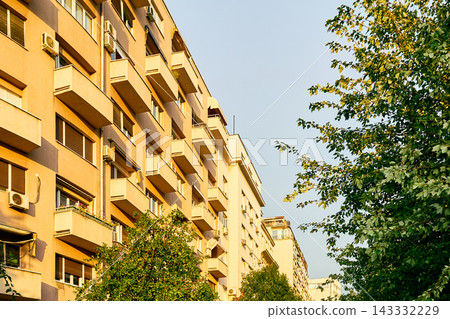 Modern apartment building facade with balconies and green trees 143332229