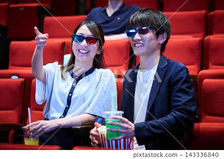 A couple enjoying a movie date at a movie theater while wearing 3D glasses. A couple enjoying a movie date at a movie theater while wearing 3D glasses. 143336840