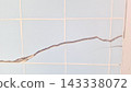 A long diagonal crack splits across the pale blue tiled wall surface 143338072