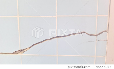 A long diagonal crack splits across the pale blue tiled wall surface A long diagonal crack splits across the pale blue tiled wall surface 143338072