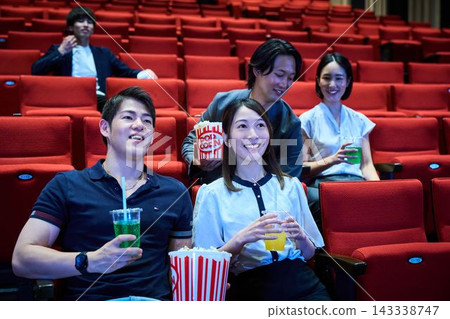 年輕人在電影院一邊吃爆米花一邊看電影。 年輕人在電影院一邊吃爆米花一邊看電影。 143338747