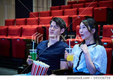 Young people enjoying watching a movie while eating popcorn at the movie theater. 143338759