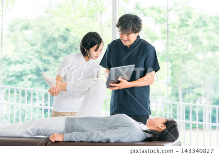 一名年輕的女員工正在接受按摩和物理治療培訓,一名男性物理治療師正在指導她。 一名年輕的女員工正在接受按摩和物理治療培訓,一名男性物理治療師正在指導她。 143340827