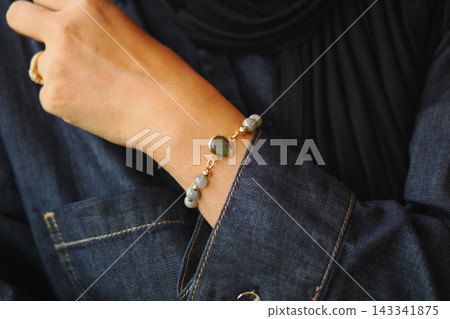 A woman shows a bracelet on their wrist while wearing a denim shirt A woman shows a bracelet on their wrist while wearing a denim shirt 143341875
