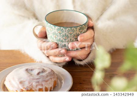 一位女士雙手捧著一杯熱騰騰的咖啡牛奶。 一位女士雙手捧著一杯熱騰騰的咖啡牛奶。 143342949