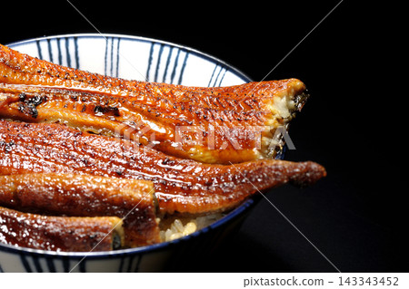 A single serving of eel rice bowl photographed against a black background. A single serving of eel rice bowl photographed against a black background. 143343452