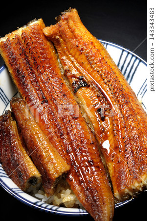 A single serving of eel rice bowl photographed against a black background. A single serving of eel rice bowl photographed against a black background. 143343483