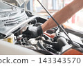 A close-up of a car mechanic's hands inspecting and repairing the engine compartment. 143343570