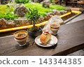 Cozy Cafe Table With Coffee Cups, Strawberry Roll Cake and Bonsai Plant Overlooking Garden 143344385