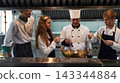 Chef teacher teaches cooking to the group children in class kitchen room. 143344884