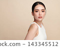 A beautiful young Asian woman with clean, fresh skin against a beige background. Skincare, facial treatment, cosmetology, beauty, and spa. An elegant portrait of an Asian woman. 143345512
