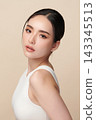 A beautiful young Asian woman with clean, fresh skin against a beige background. Skincare, facial treatment, cosmetology, beauty, and spa. An elegant portrait of an Asian woman. 143345513