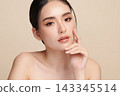 A beautiful young Asian woman with clean, fresh skin against a beige background. Skincare, facial treatment, cosmetology, beauty, and spa. An elegant portrait of an Asian woman. 143345514