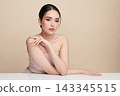 A beautiful young Asian woman with clean, fresh skin against a beige background. Skincare, facial treatment, cosmetology, beauty, and spa. An elegant portrait of an Asian woman. 143345515