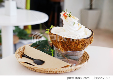 Fresh Coconut ice cream, a Thai dessert, served in a coconut shell with tropical leaf in woven basket in a cafe Fresh Coconut ice cream, a Thai dessert, served in a coconut shell with tropical leaf in woven basket in a cafe 143347928