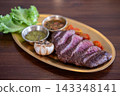 Sliced medium rare tenderloin steak served on a plate with whole cloves of roasted garlic. 143348141