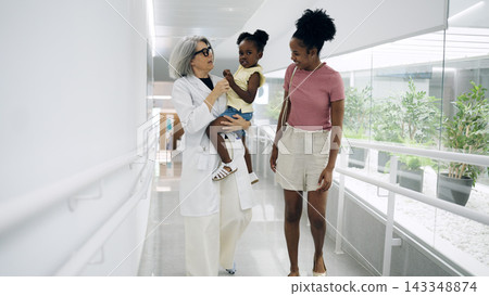 Pediatrician carrying child walking with mother in hospital Pediatrician carrying child walking with mother in hospital 143348874