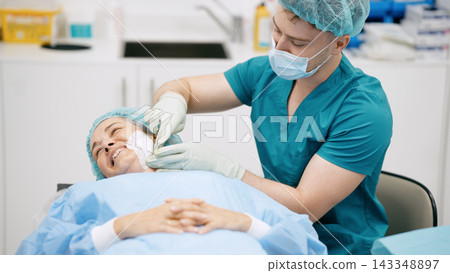 Surgeon applying bandage on patient face after cosmetic surgery Surgeon applying bandage on patient face after cosmetic surgery 143348897