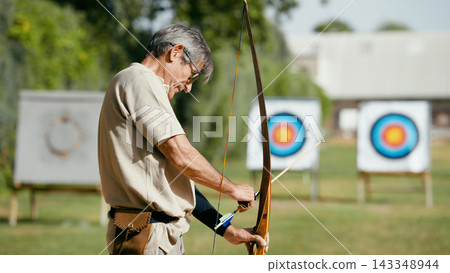 Older man practicing archery aiming for targets Older man practicing archery aiming for targets 143348944