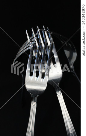Silvery identical forks linked together isolated on black backdrop Silvery identical forks linked together isolated on black backdrop 143348970