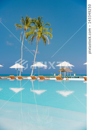 Inviting infinity pool umbrellas leaning palms vivid turquoise lagoon blue sky bright Maldives resort. Luxury five star spa retreat. Exclusive indulgent poolside stay 143349250