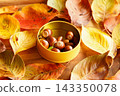 Autumn leaves spread across a wooden table, and acorns in a yellow round can. 143350078