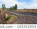 Winding Asphalt Desert Highway with Guardrail and Eucalyptus Trees near Matmata Arid Landscape 143352854