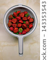Fresh ripe strawberries in a plastic colander on a marble countertop, top view. 143353543