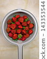 Fresh ripe strawberries in a plastic colander on a marble countertop, top view. 143353544