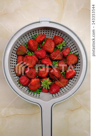 Fresh ripe strawberries in a plastic colander on a marble countertop, top view. Fresh ripe strawberries in a plastic colander on a marble countertop, top view. 143353544