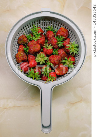 Close up of ripe strawberries soaking in water inside a colander. Close up of ripe strawberries soaking in water inside a colander. 143353548