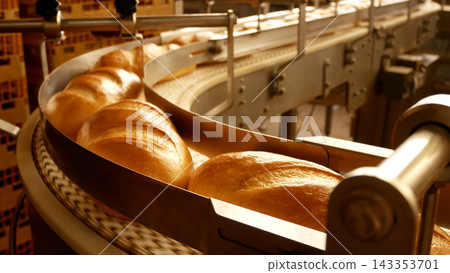 Industrial conveyor line in a bakery with freshly baked baguettes moving from the oven. Industrial conveyor line in a bakery with freshly baked baguettes moving from the oven. 143353701